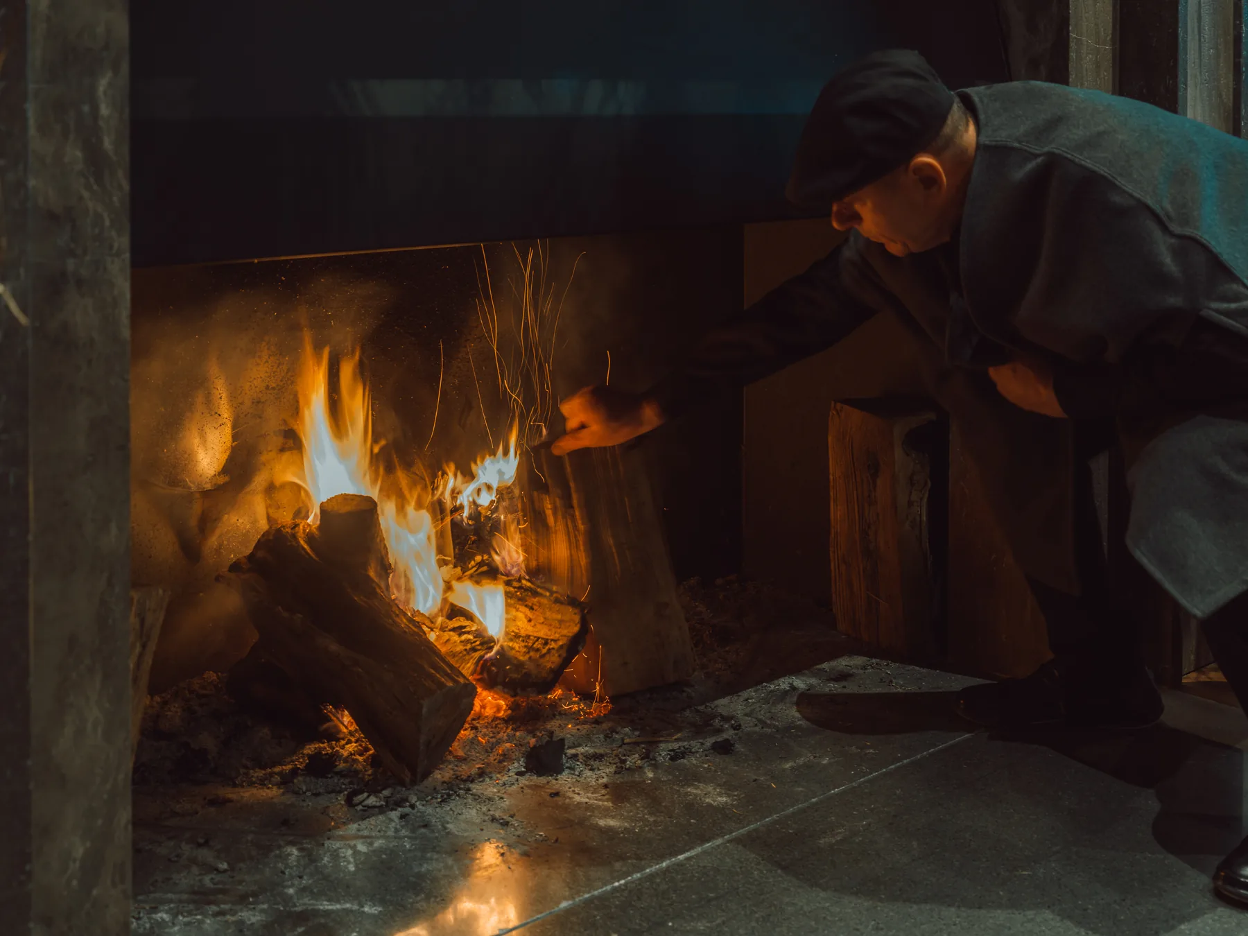 Logs burning in MANNA's open fireplace as a hand tends the fire