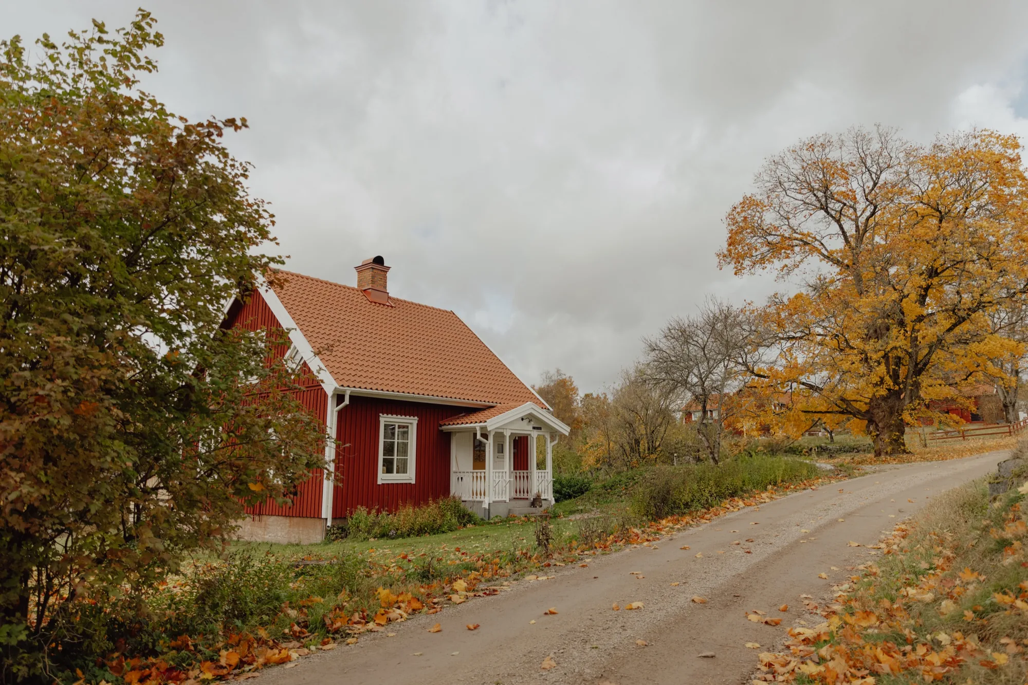 Classic red Swedish farmhouse with a white gable and veranda beside an autumn road