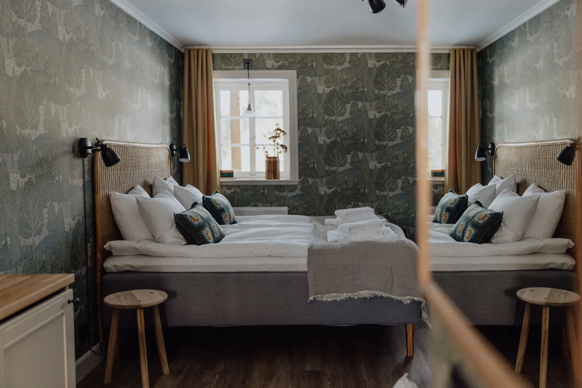 Farmstead bedroom with leaf-patterned wallpaper, twin rattan beds and yellow curtains